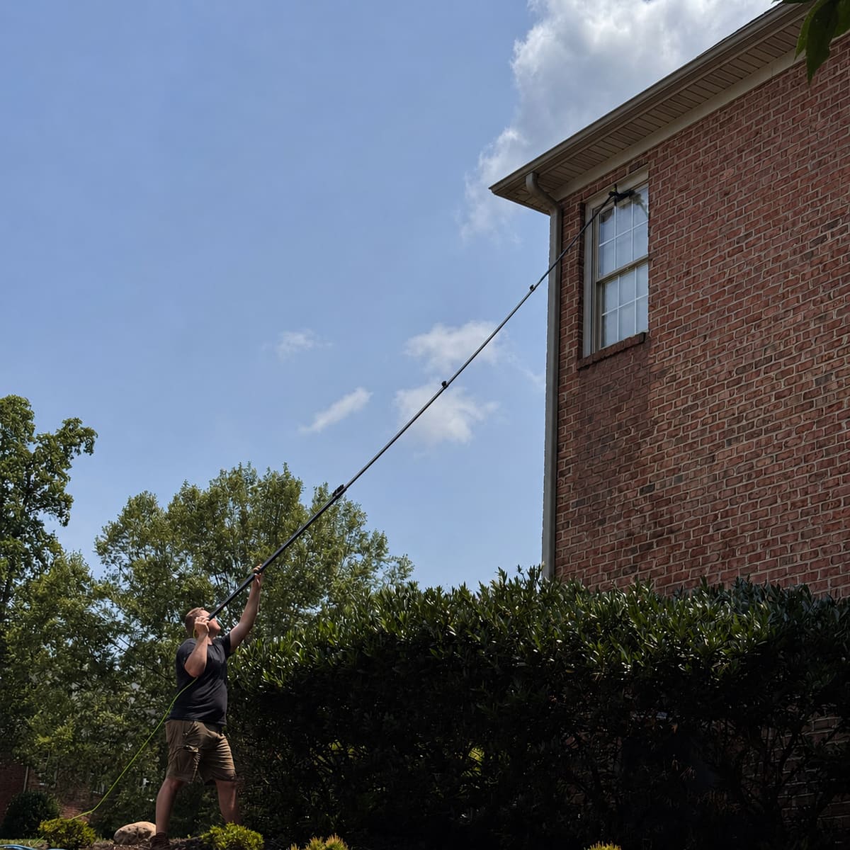 ViewPoint LLC technician cleaning second-story windows of a brick Lynchburg area home with a water-fed pole