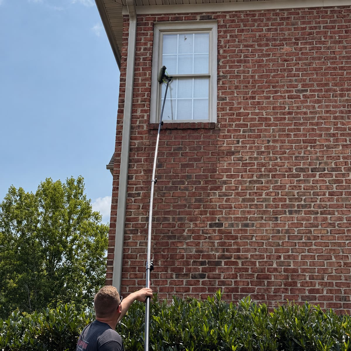 ViewPoint LLC technician washing second-story windows of a brick home with a water-fed pole brush
